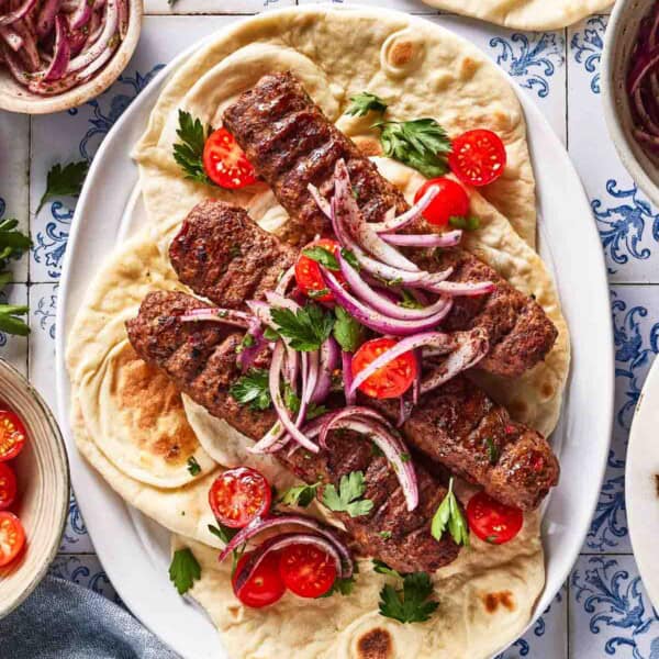 Adana kebab garnished with sumac onions and tomatoes on a plate.