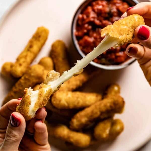 A person pulling apart a breaded cheese stick from the top view.