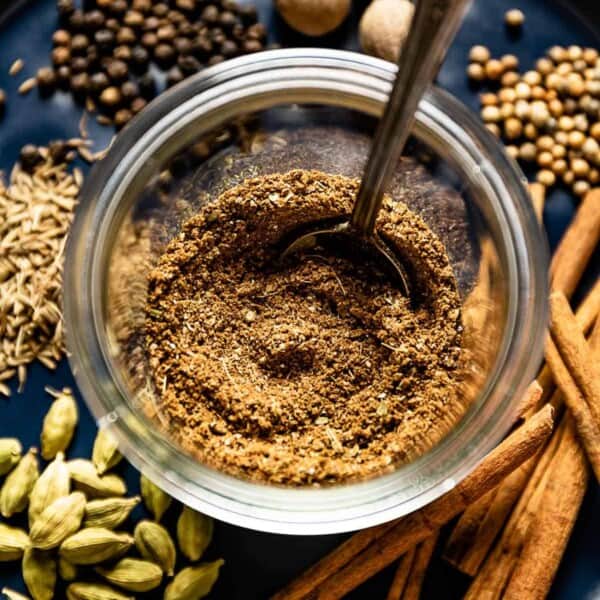 Baharat Spice Mix in a glass jar with a spoon in the jar.