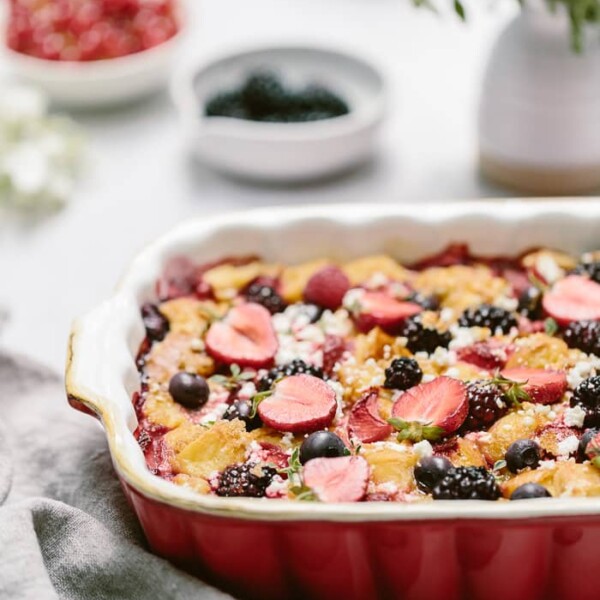 Goat cheese bread pudding with berries in a casserole dish with flowers in the background.