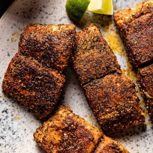 Blackened mahi mahi fillets on a plate with lime wedges on the side.