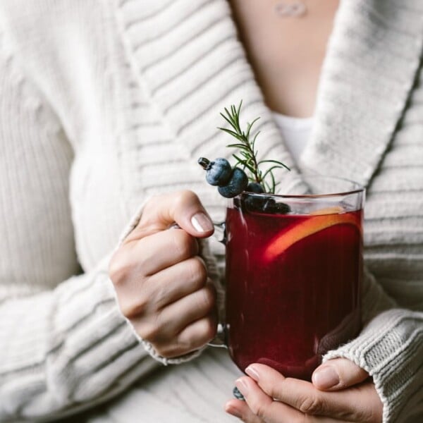 A woman holding a glass of Honey Sweetened Blueberry Hot Toddy: This easy-to-make blueberry hot toddy is the best way to warm yourself in these cold winter days.