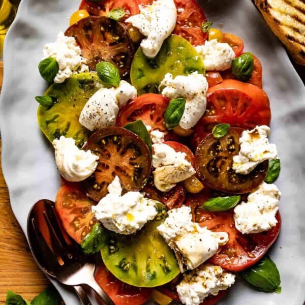 Burrata Caprese with tomatoes. basil and burrata cheese styled on a plate from the top view.