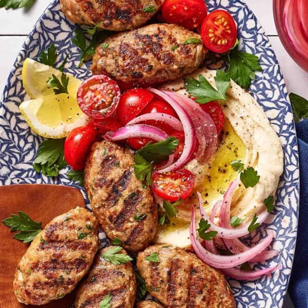 Chicken kofta on a platter with hummus and red onions.