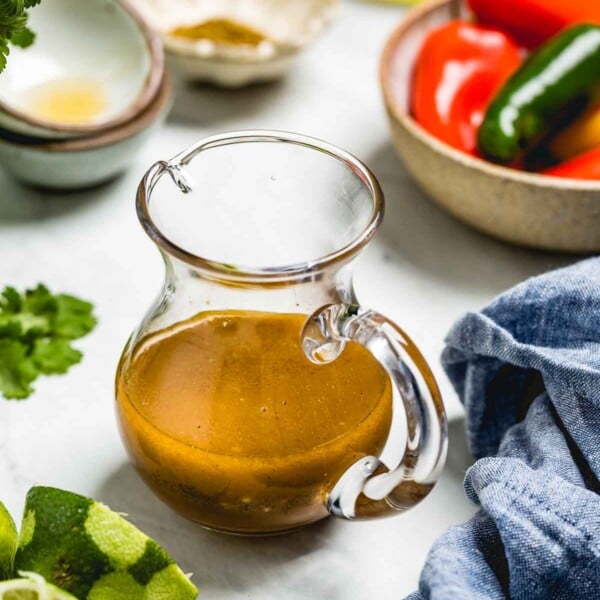 A small jug of chili lime vinaigrette recipe is photographed from the front view with vegetables around it.
