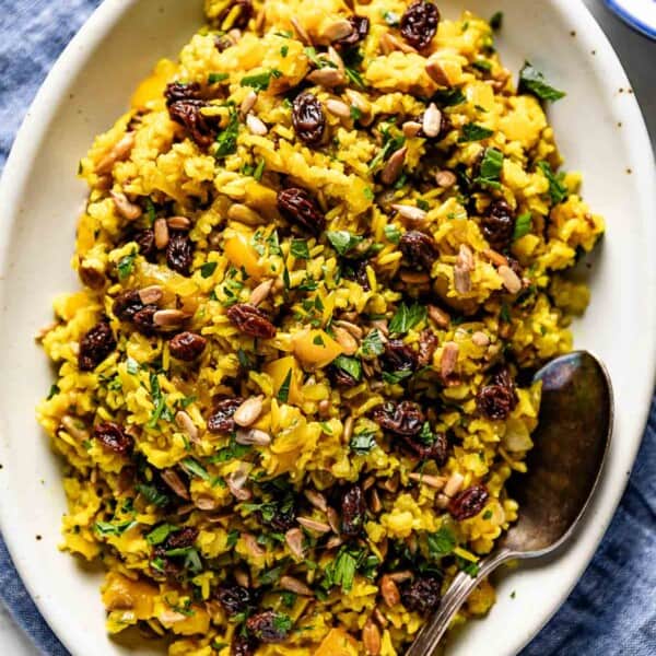 Curried brown rice on a plate garnished with raisins and sunflower seeds.
