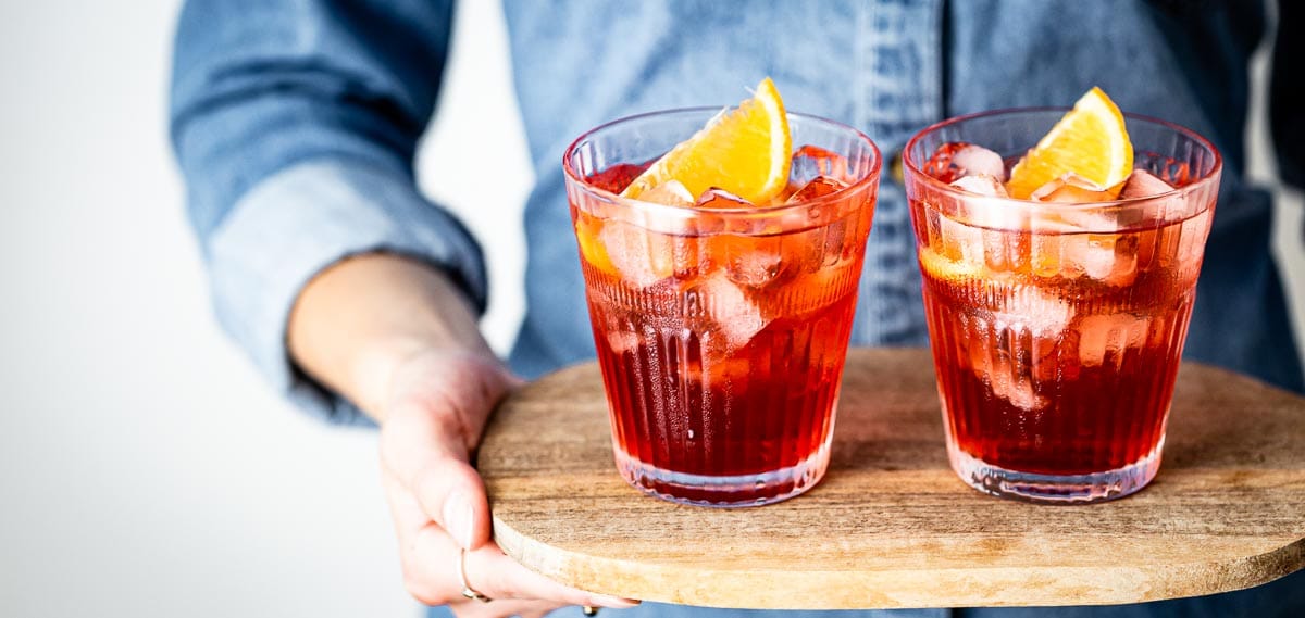 A woman is holding two glasses cocktails in her hand