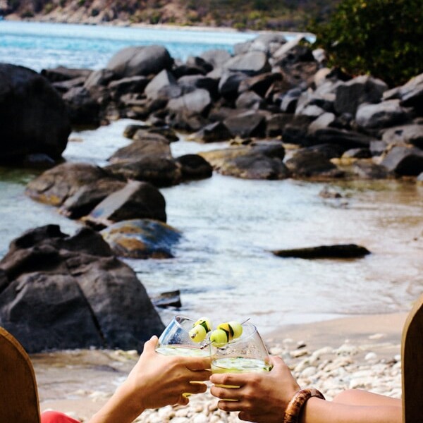Two people sitting on a beach holding two Women on the Rock A Caribbean Cocktail