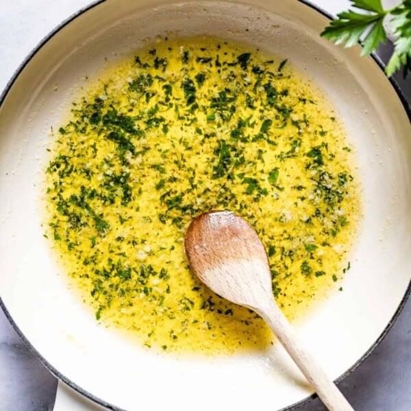 Garlic butter sauce garnished with parsley in a skillet with a wooden spoon.