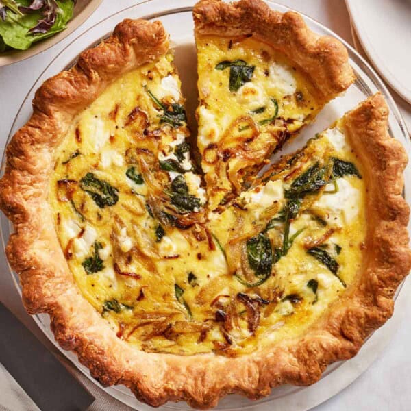 Goat cheese quiche with caramelized onion and spinach in a pie plate.