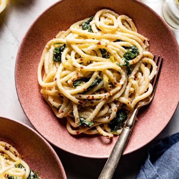 Lemon ricotta pasta in a bowl with glasses and seasoning on the side