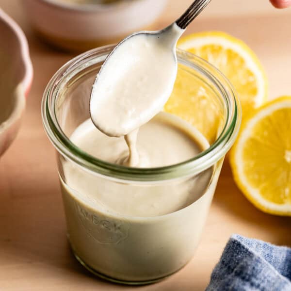 Lemon tahini sauce with a spoon in a jar from the front view.
