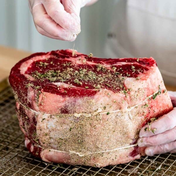 Prime rib seasoning being sprinkled over a standing rib roast.