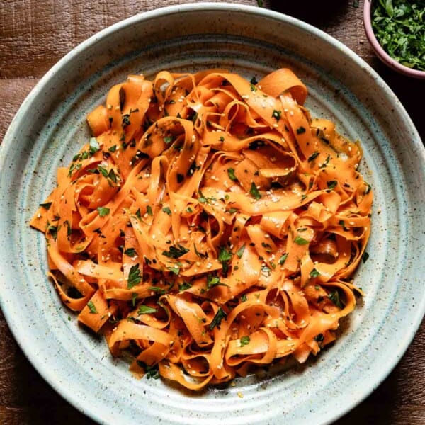 Raw carrot salad in a bowl garnished with sesame seeds and parsley.