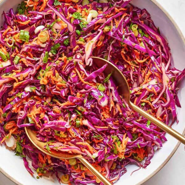 Red cabbage coleslaw in a bowl with utensils from the top view.