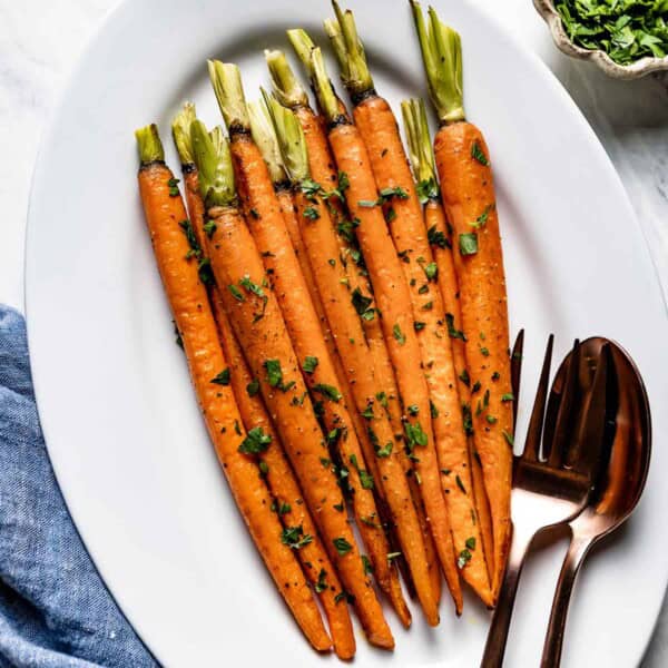 Roasted whole carrots garnished with parsley on a plate.