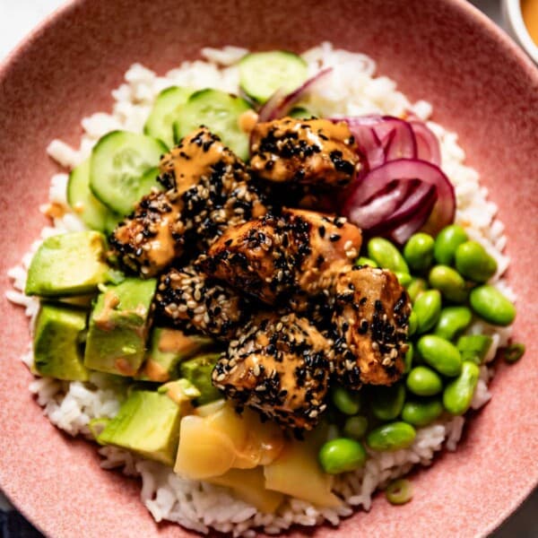 A bowl of rice topped off with veggies and sesame crusted salmon from the top view.