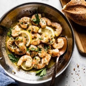 A skillet filled with juicy shrimp, lemon slices, and fresh parsley. This date night food is quick and easy to prepare.
