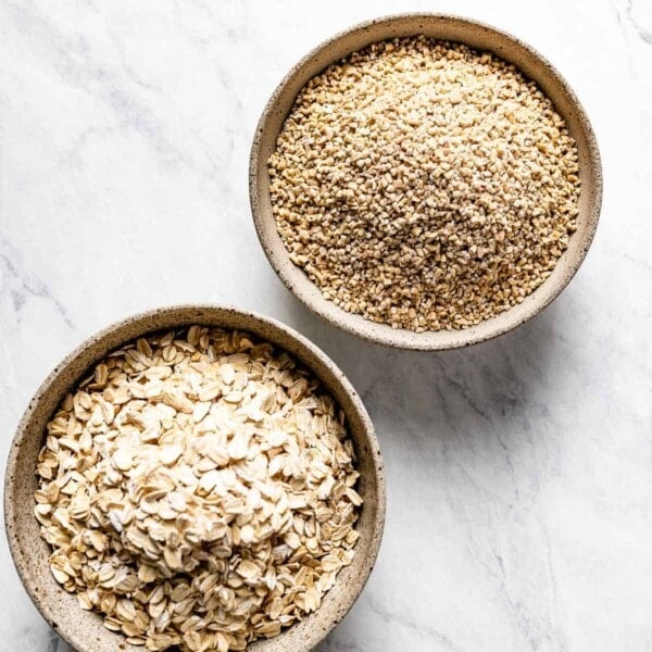 steel cut oats and rolled oats in small bowls on a marble backdrop.