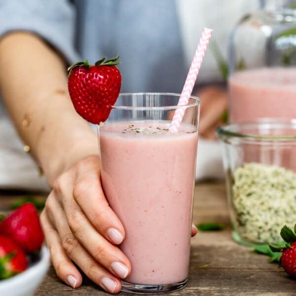A person is serving a strawberry banana smoothie with yogurt in a glass.