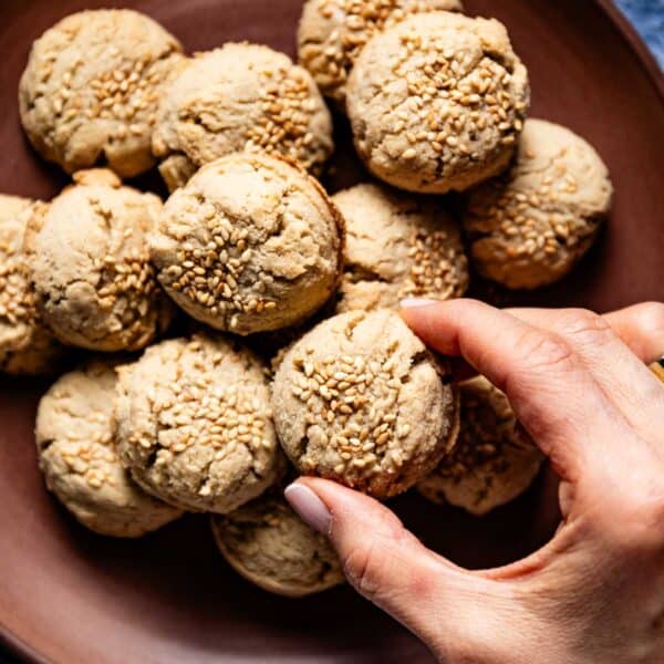 Almond flour tahini cookies on a plate from the top view with a person taking one from the plate.