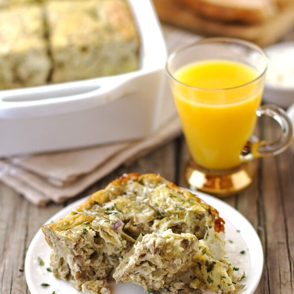 A serving Eggs with Artichoke, Tarragon, and Parmesan with a glass of orange juice and a platter of the dish in the background