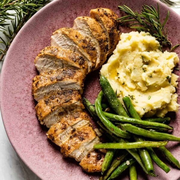 Sliced turkey tenderloin on a plate with vegetables from the top view.