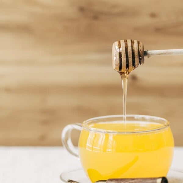 A glass cup full of turmeric ginger tea is being drizzled with honey photographed from the front view.