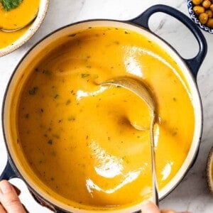Sweet potato soup in a pot being mixed with a ladle.
