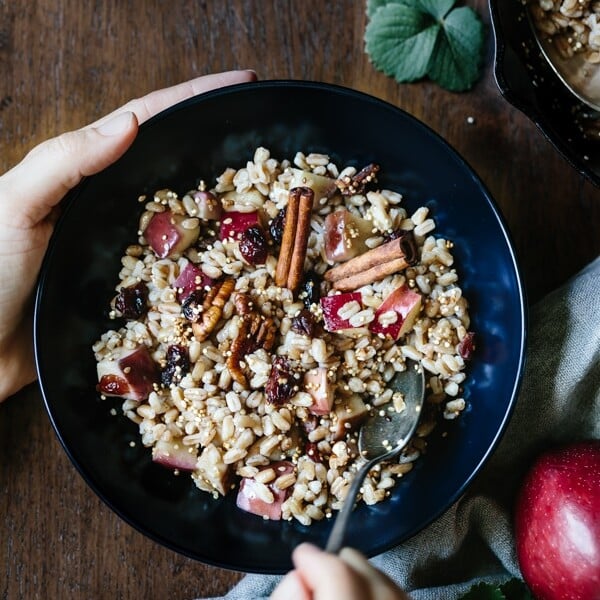 A woman is dipping her spoon in a warm farro breakfast