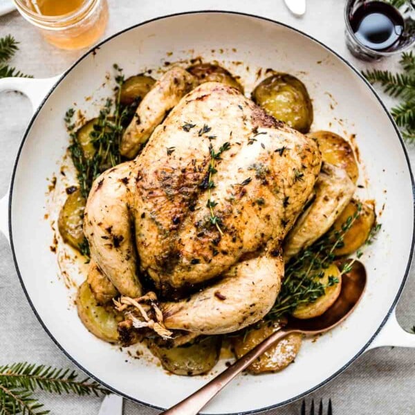 Whole roasted chicken with potatoes in a skillet with a spoon on the side